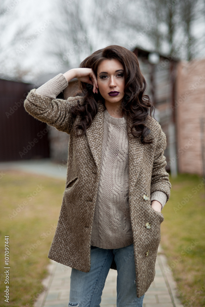 Spring in the country style. Full length portrait of young woman in white knitted sweater and furry hat standing in the front of rustic wood wall in the yard near house, wearing sweater casual. Spring in the country style. Full length portrait of young woman in white knitted sweater and furry hat standing in the front of rustic wood wall in the yard near house, wearing sweater casual.