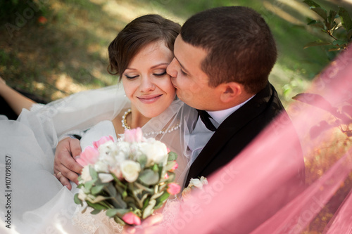 Canvastavla Elegant young happy wedding couple is sitting at green grass on