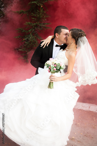 Elegant young happy wedding couple is sitting at green grass on