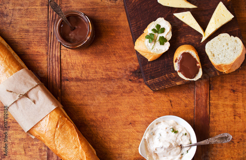 Savory and sweet snacks with French baguette on a wooden table, top view