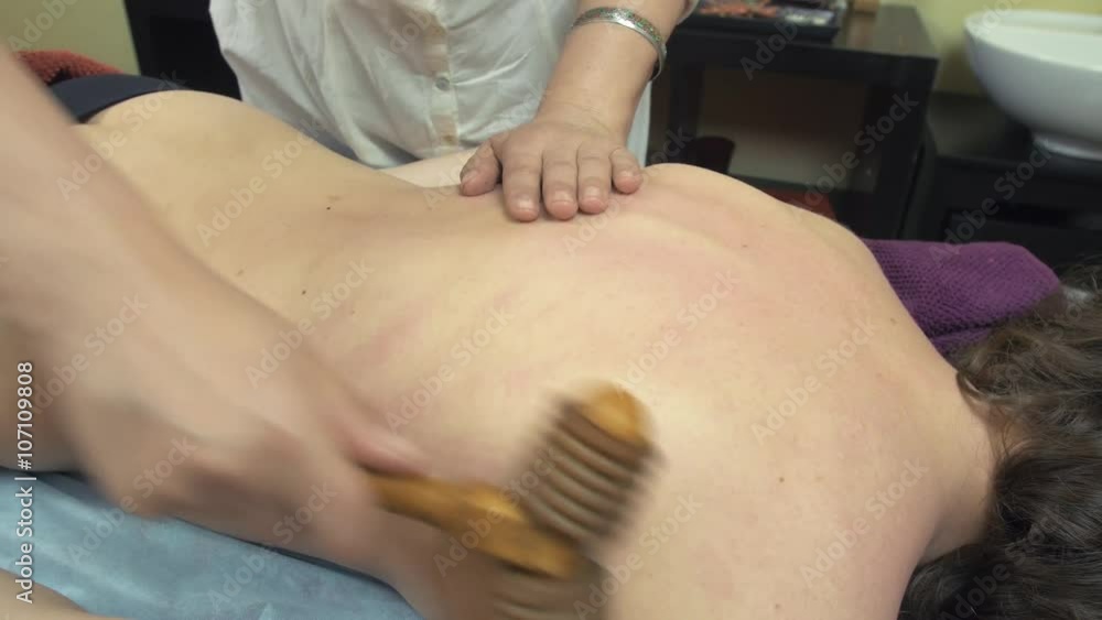 Close up of masseuse make healing massage of backbone by wooden massage roller to woman in saloon. Close up of masseuse make healing massage of backbone by wooden massage roller to woman in saloon.