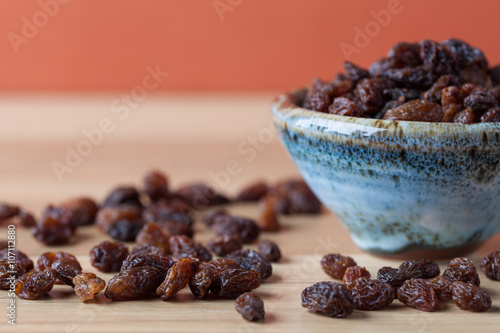 Organic raisins in handmade ceramic bowl on wooden table. Horizontal image with copy space. Shallow depth of field.