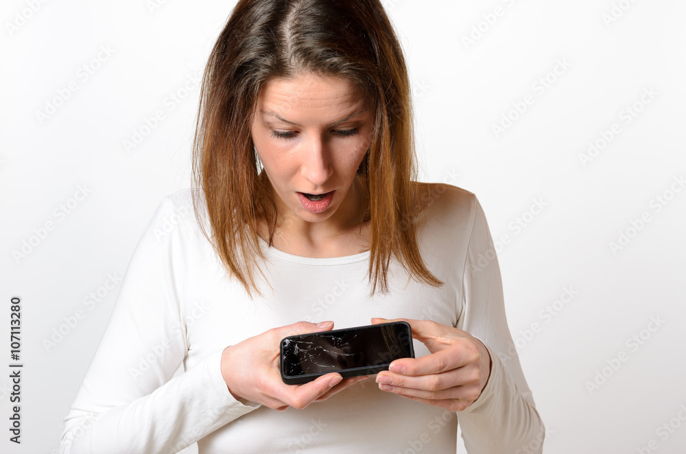 Surprised woman looks down at broken mobile phone Surprised woman looks down at broken mobile phone
