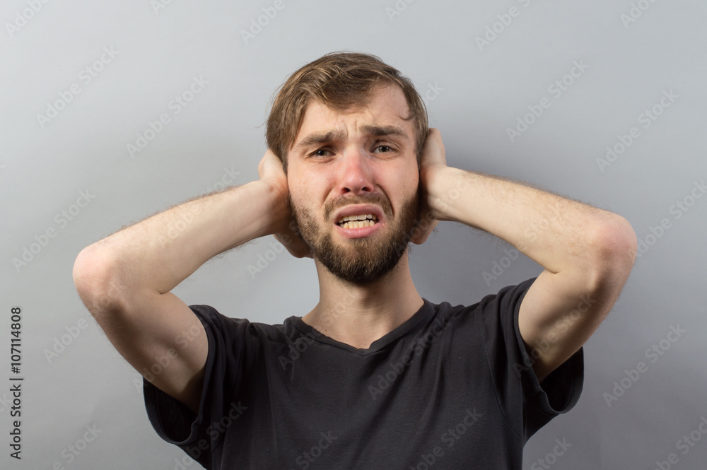 stressed young man close his ears and eyes on grey background
