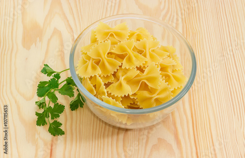 Uncooked bow-tie pasta in glass bowl, sprig of parsley