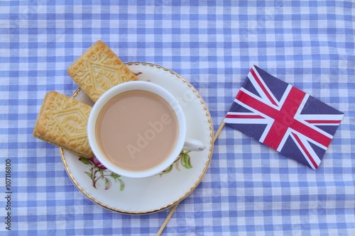 Traditional milky tea served in a bone china cup and saucer with custard cream type biscuits with a Union Jack flag 