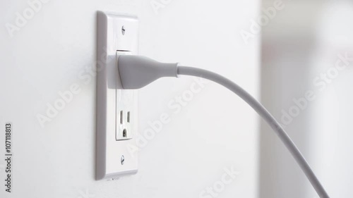 Close up of a hand plugging in a power cord and then unplugging it in a typical electrical outlet cover in the USA.  Originally recorded in 4K
