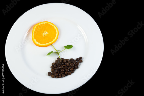 Concept for smart eating with flower made from slice of orange on the top, lemon balm as stalk and coffee beans as soil, on white plate and black background