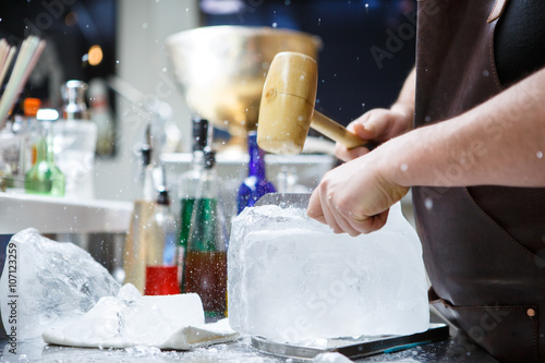 Bartender mannually crushed ice with wooden hammer and metal knife. © Sergey