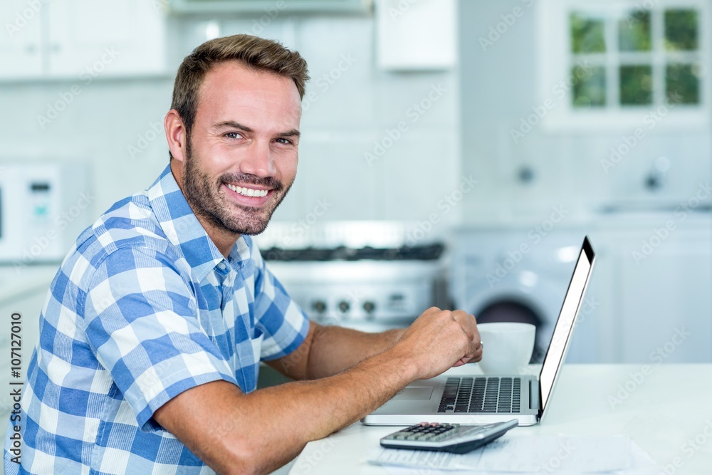 Happy handsome man using laptop at table in kitchen Happy handsome man using laptop at table in kitchen