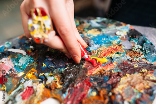 Painter mixes yellow and red oil paint on the old palette. Closeup of paint mixing process in art workplace. Painter preparing to paint.