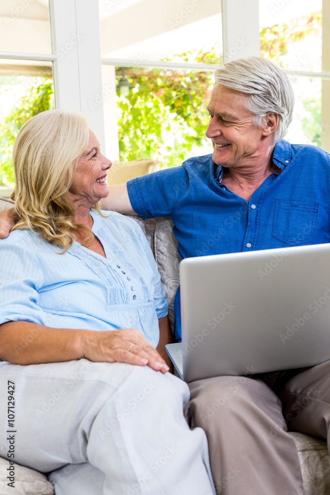 Obraz premium Happy senior couple with laptop while sitting on sofa at home