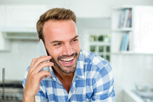 Happy handsome man talking on cellphone in kitchen