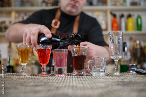 Bartender pours various of alcohol drink into small glasses on bar