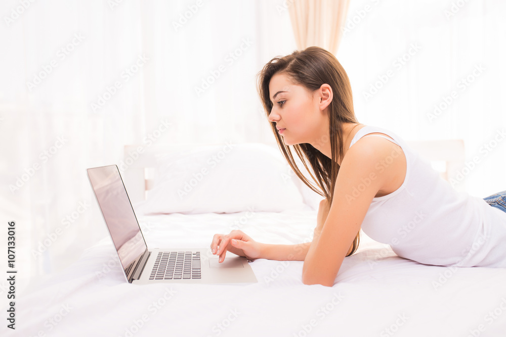pretty girl looking at laptop monitor while lying on bed in her room pretty girl looking at laptop monitor while lying on bed in her room