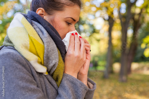 Young girl is blowing her nose. She is cold. Autumn time.