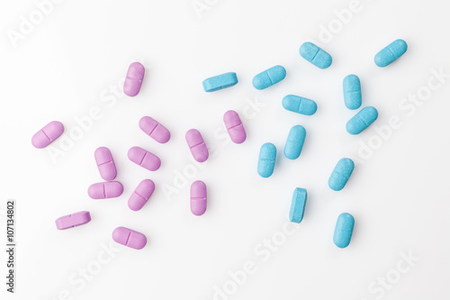 Scattered pink and blue pills on white background directly from above