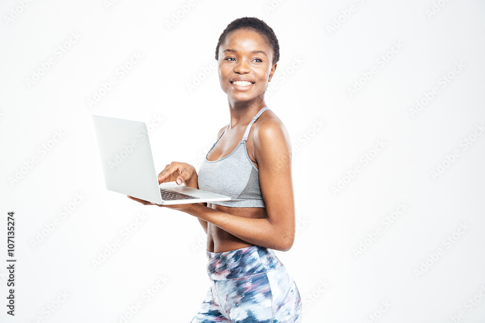 Cheerful beautiful young african american sportswoman standing and using laptop Cheerful beautiful young african american sportswoman standing and using laptop