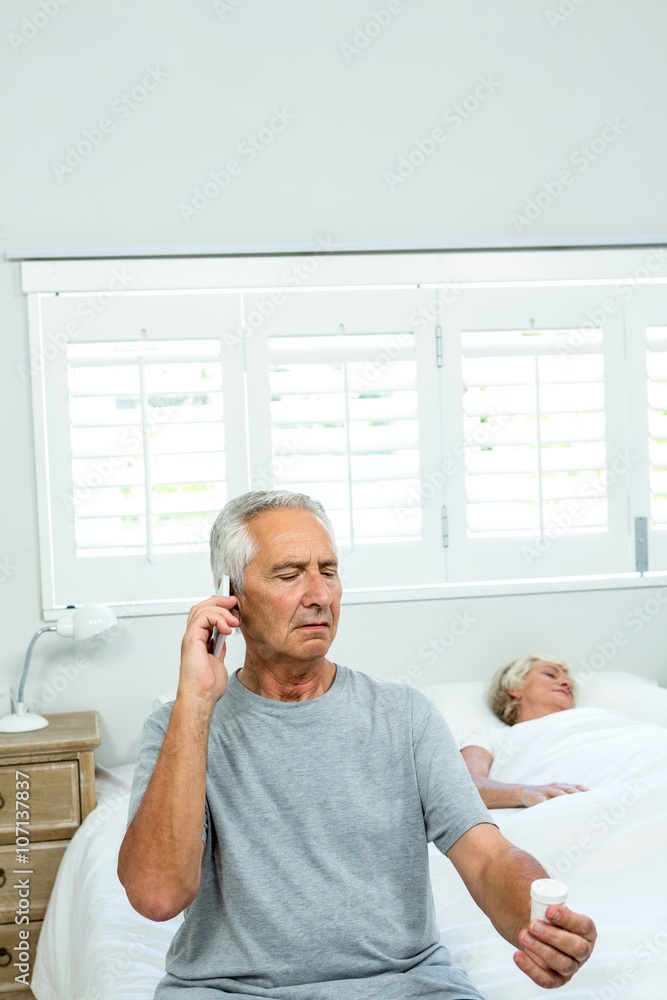 Old man talking on phone with woman sleeping on bed at home