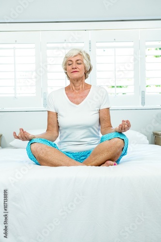 Aged woman doing yoga on bed