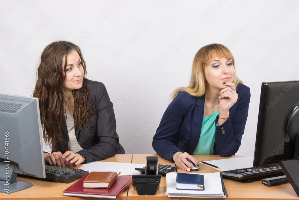 Office worker looking with distaste at the colleague sitting next to staring at a computer monitor Office worker looking with distaste at the colleague sitting next to staring at a computer monitor