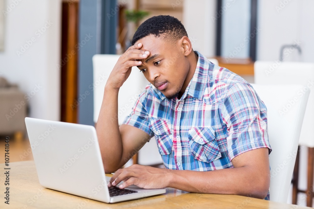 Tense young man using laptop in kitchen