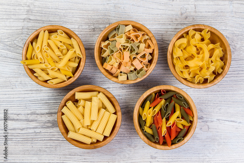 Various combinations of pasta on wooden background, burlap bags, bamboo bowls. diet and nutritional concept.