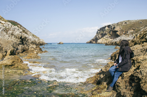 Woman in front of the sea sitting on the rocks