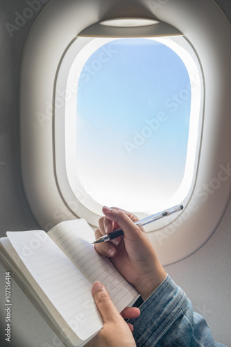 Woman writing on blank notebook while travelling on plane.