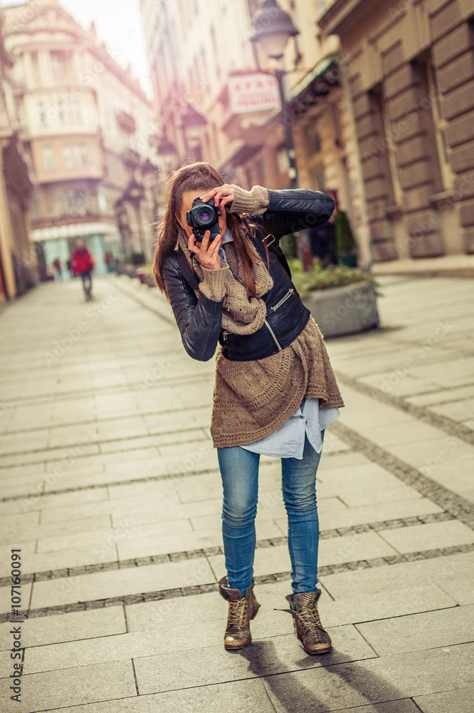 Pretty young female tourist photographer taking pictures in the city