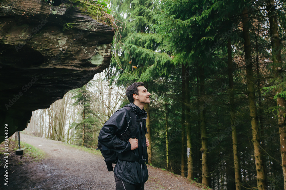 Young Man,Student hiking in forest.Man hiker smiling happy portrait looking up enjoying nature on foggy day during a trekking trip. Back of a young man outdoors in nature on a hiker path in forest.