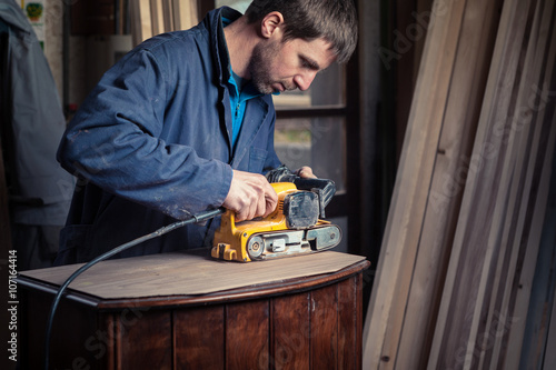 Carpenter restoring furniture with belt sander photo