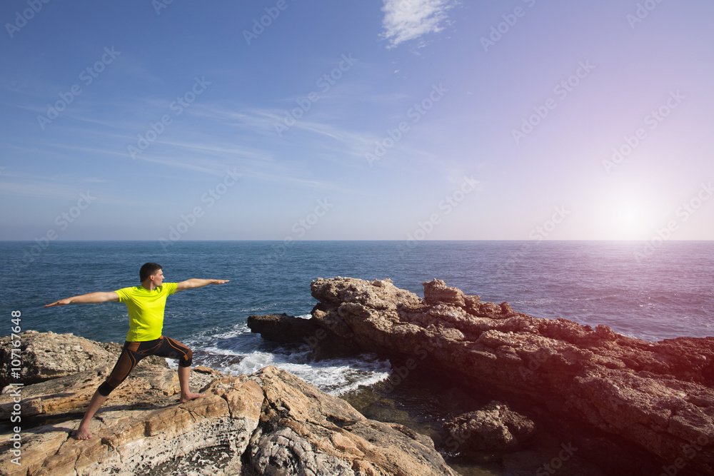 Young man practicing yoga on the beach.