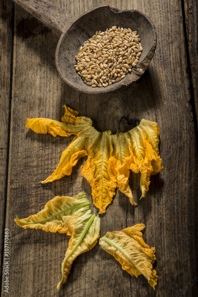 fiori di zucca con mestolo in legno contenente grano su tavolo in legno scuro fiori di zucca con mestolo in legno contenente grano su tavolo in legno scuro