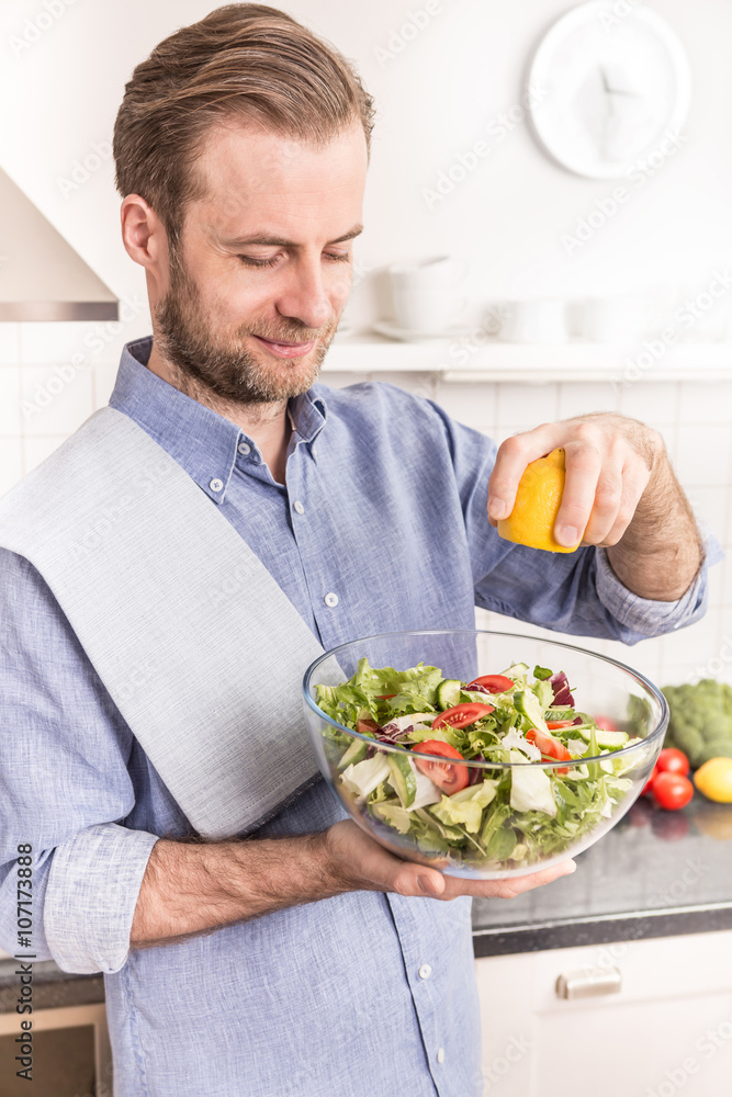 Happy smiling man making fresh vegetable salad in the kitchen Happy smiling man making fresh vegetable salad in the kitchen