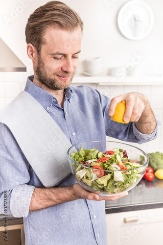 Happy smiling man making fresh vegetable salad in the kitchen