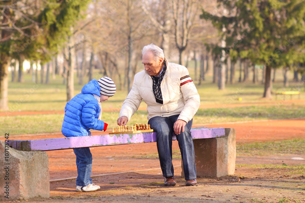 Grandfather and grandson playing chess on a bench outdoors Grandfather and grandson playing chess on a bench outdoors