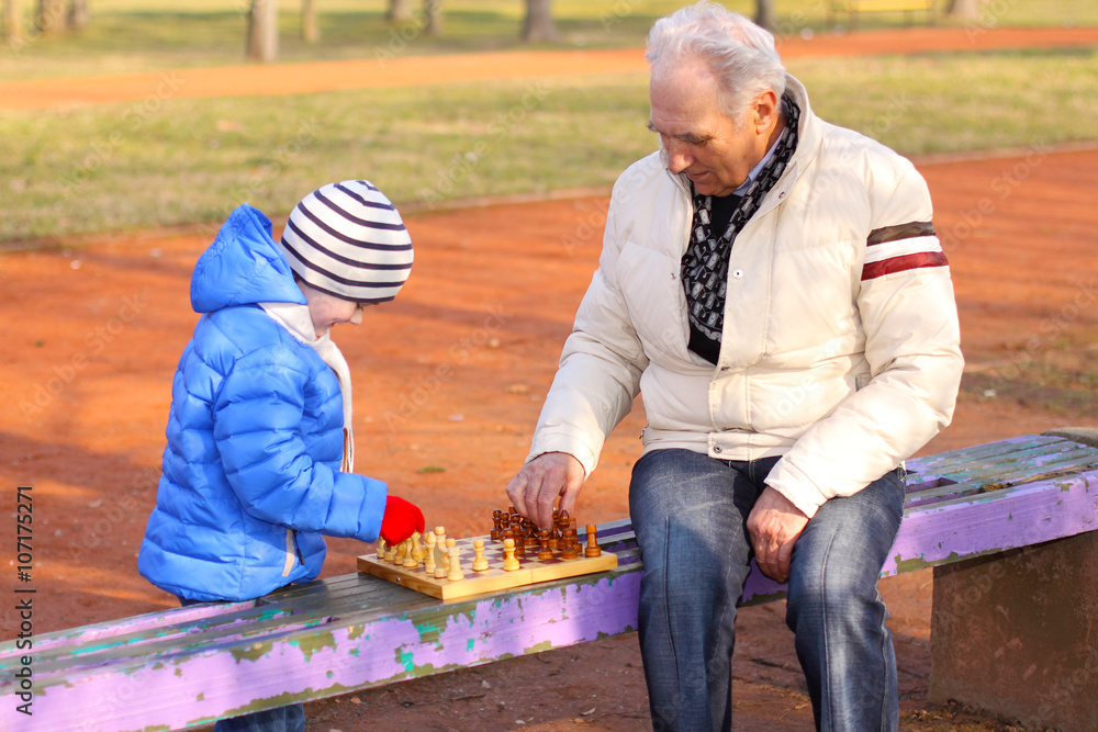 Grandfather and grandson playing chess on a bench outdoors Grandfather and grandson playing chess on a bench outdoors