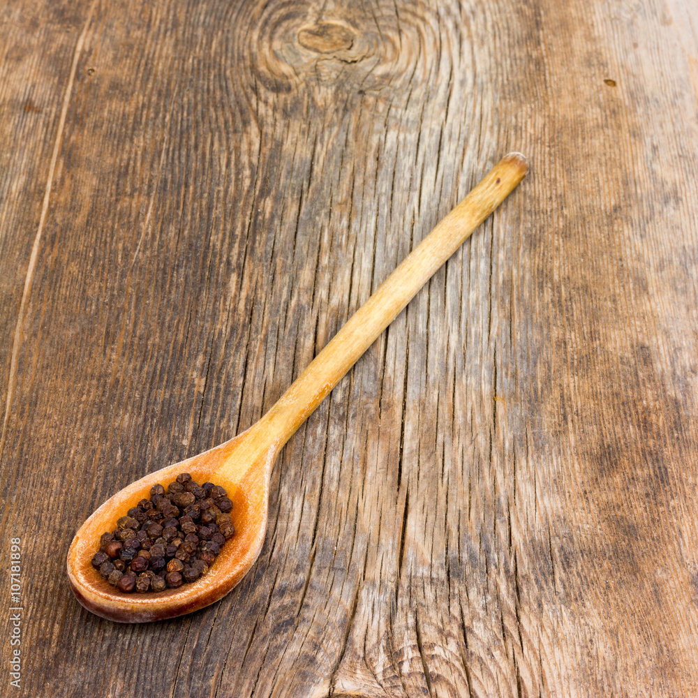 black pepper in a wooden spoon on the old cracked board. Selective focus. square photo