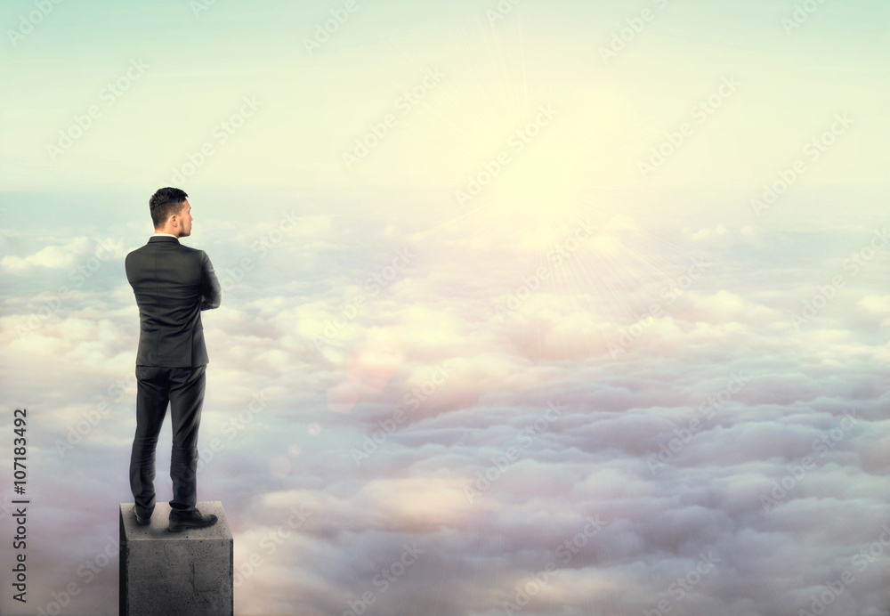 Young man in business suit, standing on concrete column above clouds. Young man in business suit, standing on concrete column above clouds.