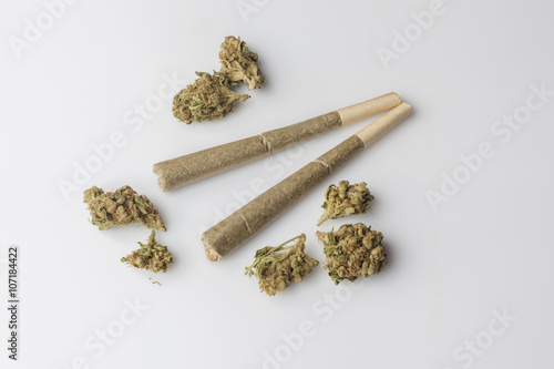 Two medical cannabis rolled joints with dried marijuana buds around on white background from above