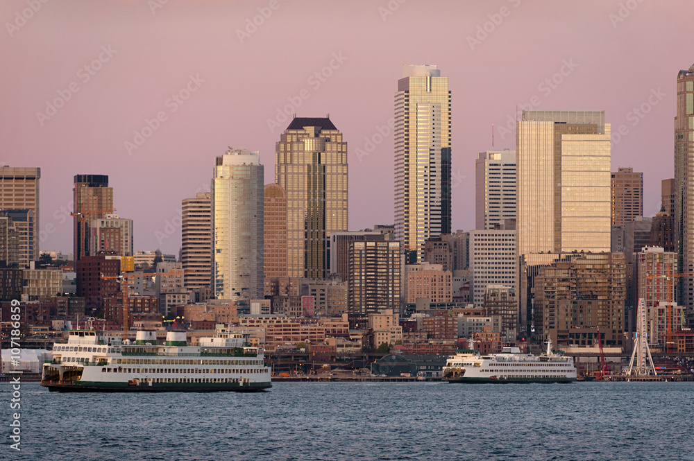 Seattle Skyline at Sunset. During a beautiful Seattle, Washington sunset ferry boats run between Bainbridge Island and downtown Seattle. Modern skyscrapers line the waterfront.