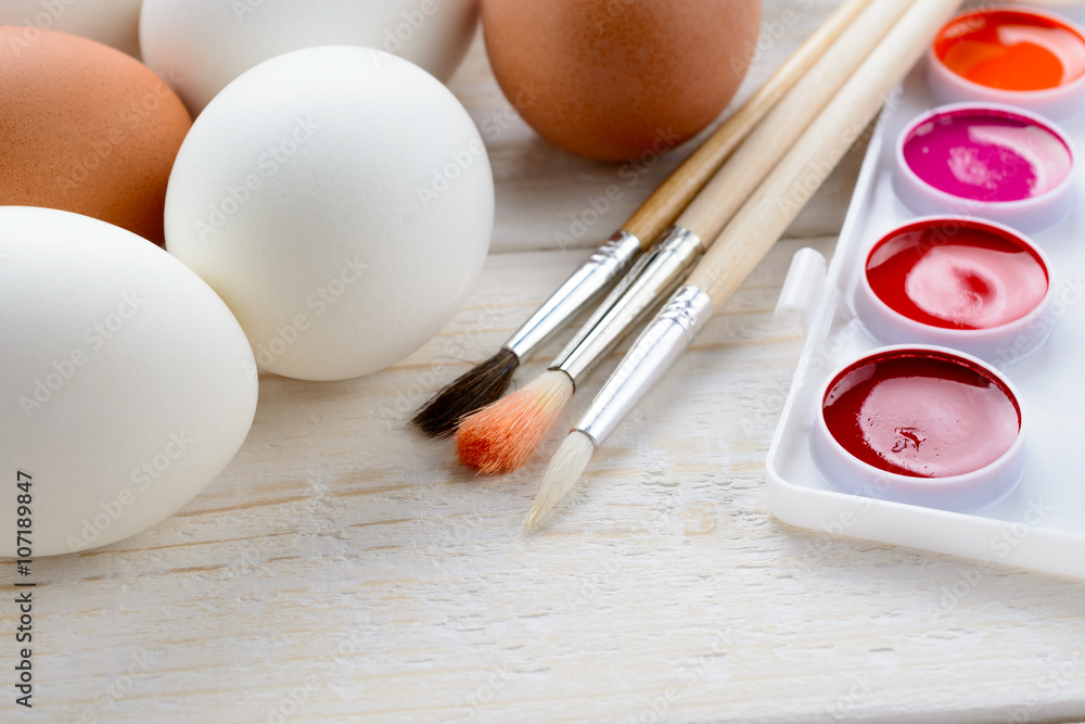 Chicken eggs and paints with brushes on the table Chicken eggs and paints with brushes on the table