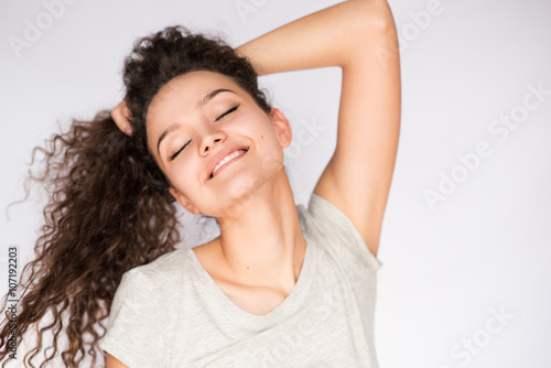 Positive and happy portrait of smiling young woman with closed eyes and playing with curly hair