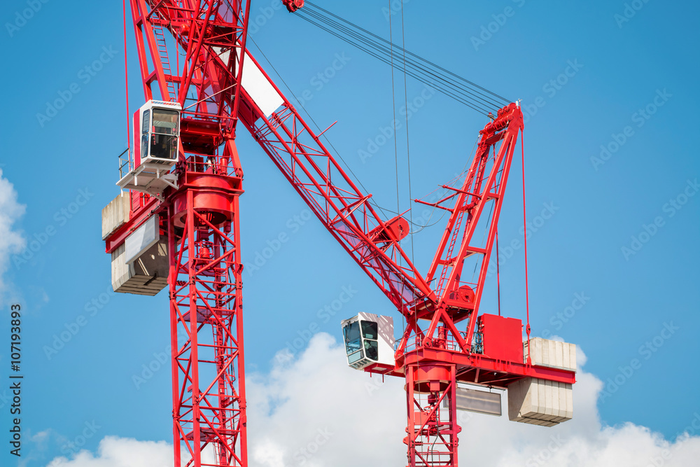 Two Red Construction Tower Cranes Against Blue Sky. Construction Industry Concept Two Red Construction Tower Cranes Against Blue Sky. Construction Industry Concept