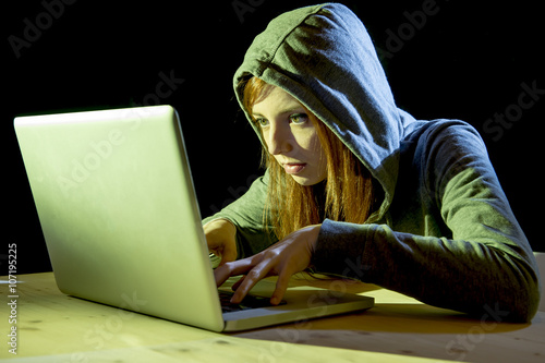 young attractive teen woman wearing hood on hacking laptop computer cybercrime cyber crime concept