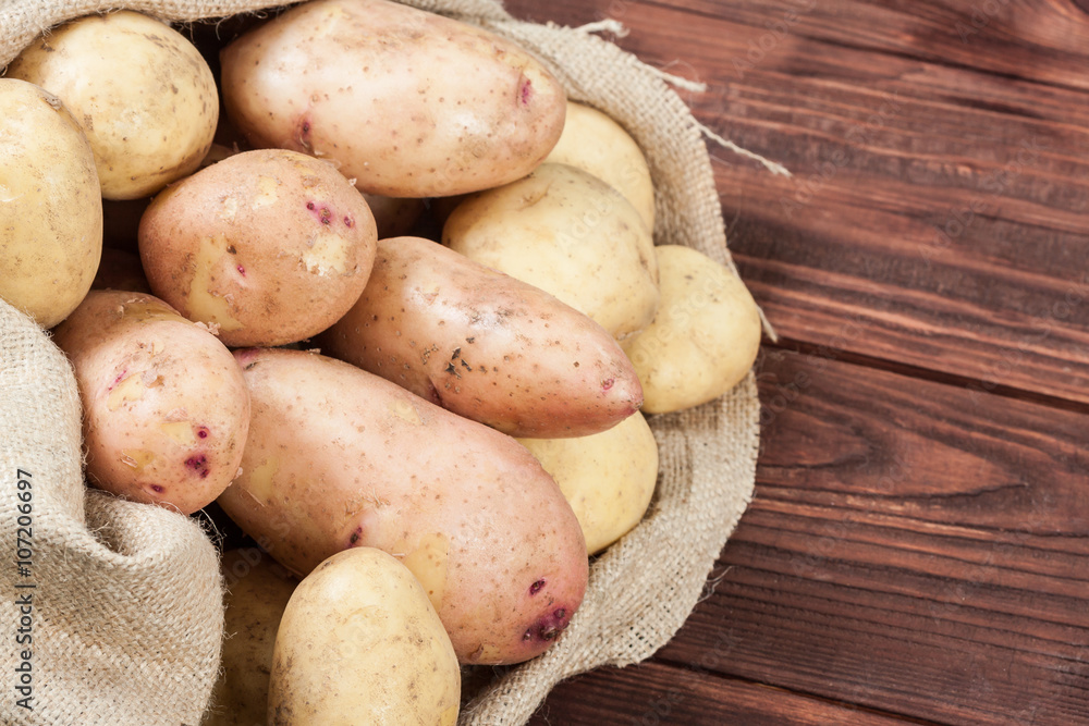 Harvest potatoes in burlap sack on wooden background Harvest potatoes in burlap sack on wooden background