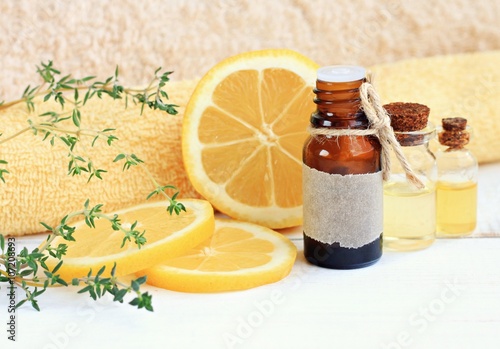 Lemon essential aroma oil. Cosmetic glass bottle, fresh fruit, thyme herb, towels.