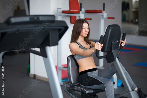 Beautiful young girl engaged in fitness in the gym. Perform cardio exercise on a simulator.