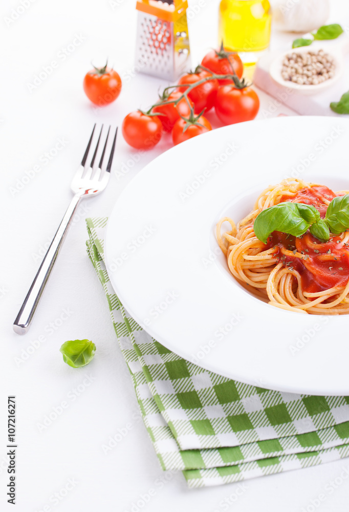 Tomato pasta spaghetti with fresh tomatoes, basil, italian herbs and olive oil in a white bowl on a white wooden background, closeup.